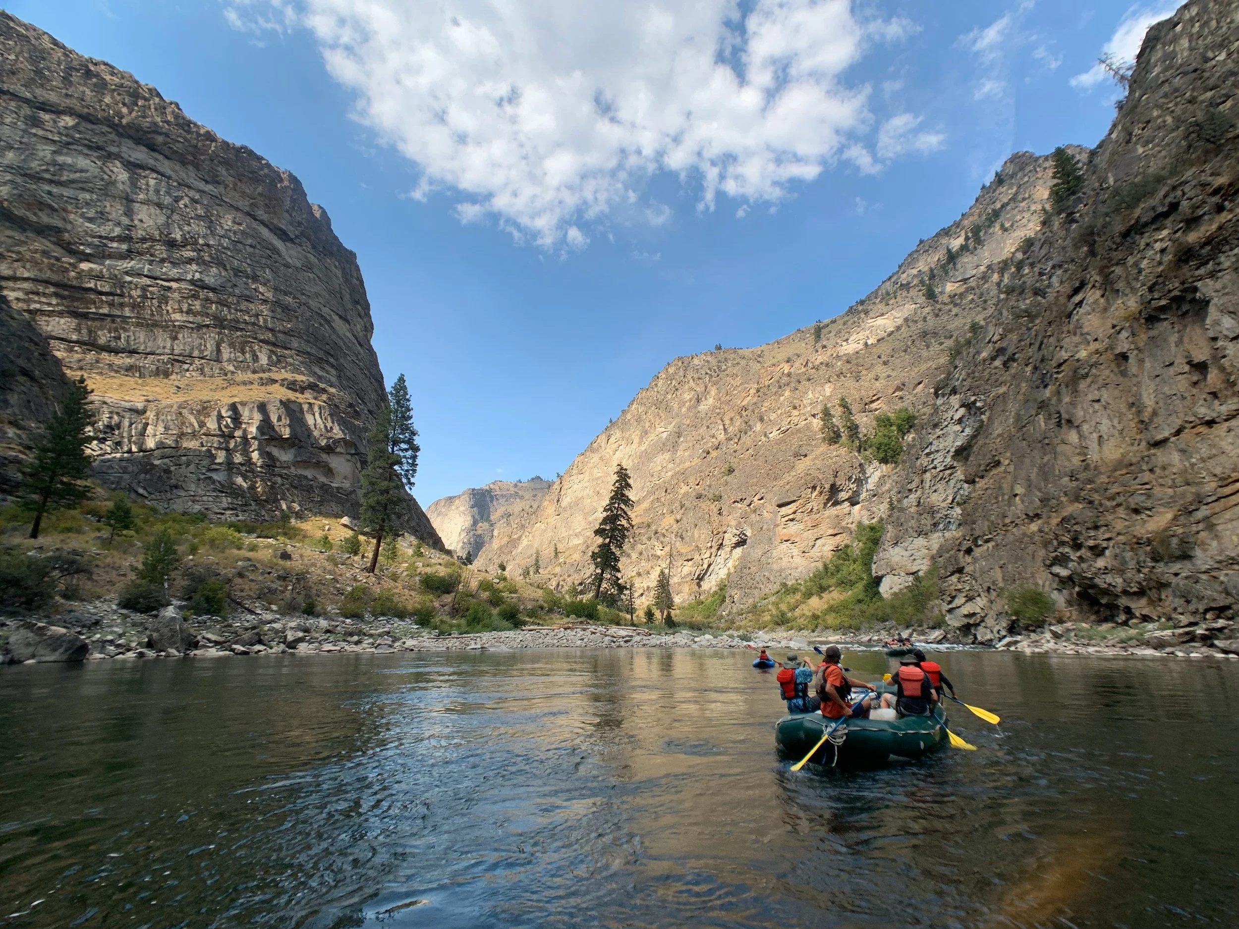A raft of people on a wild river beneath tall canyon walls.