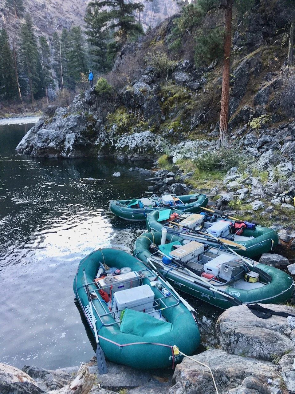 Loaded rafts tied up on a rocky riverbank.